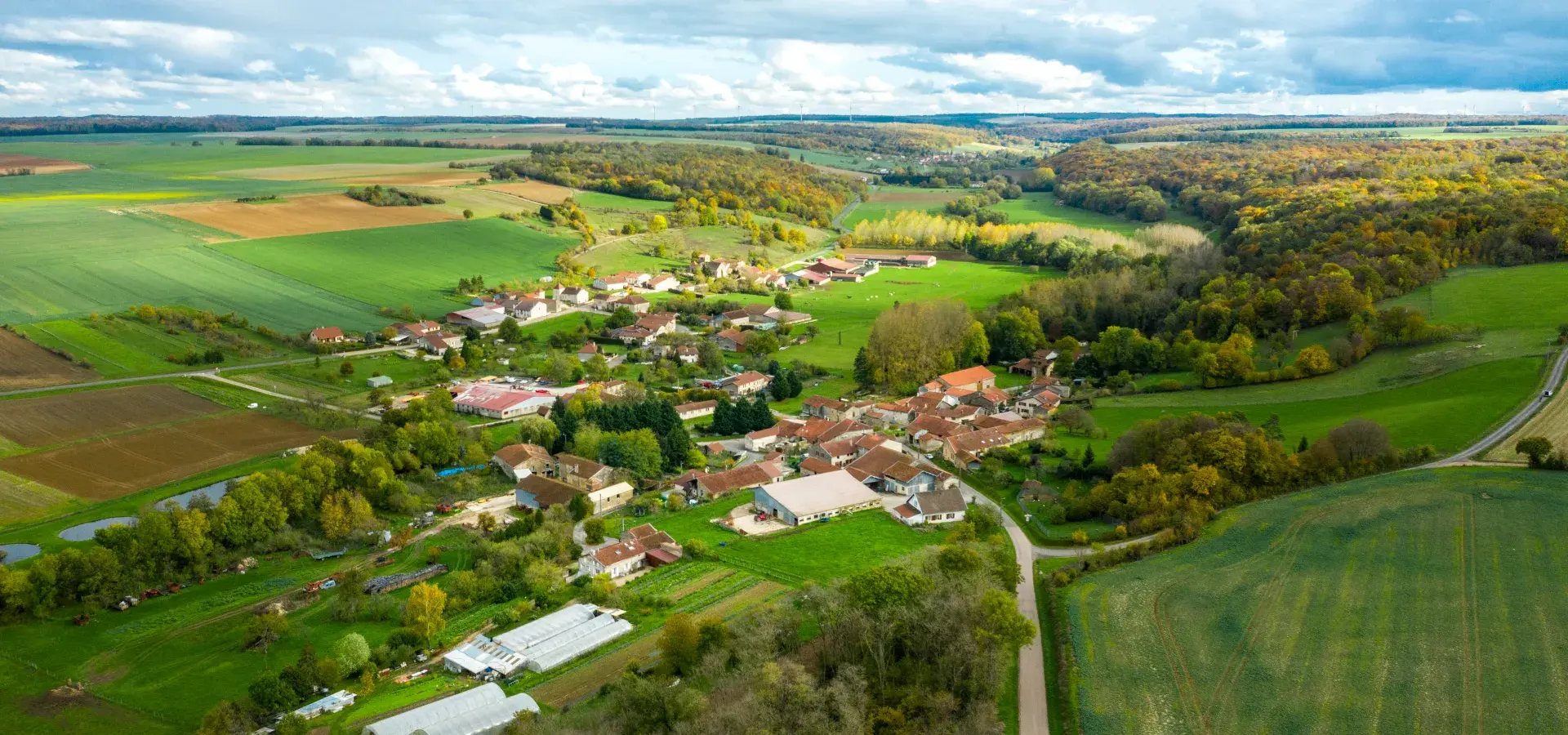 Photo aérienne d'une commune française avec quelques éoliennes visibles à l'horizon et des champs agricoles au premier plan