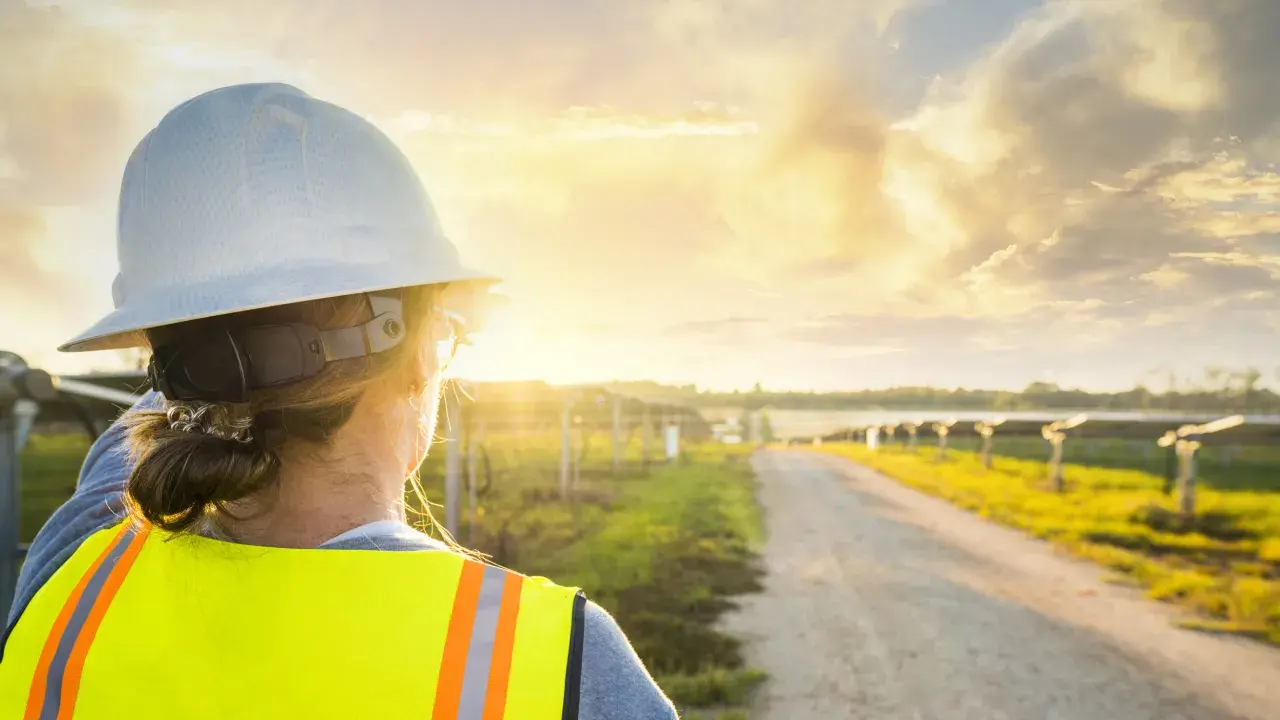 Technicienne faisant face à des panneaux solaires et un couché de soleil